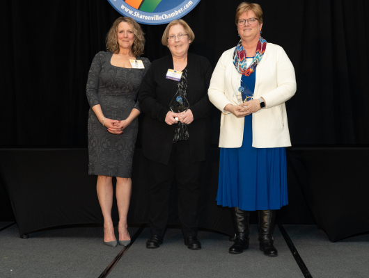 three women standing together as two are holding awards