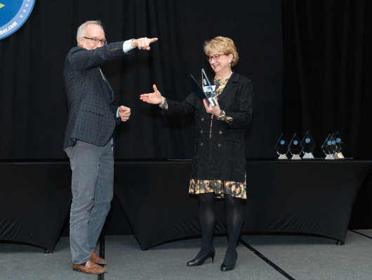 man on stage pointing  and woman on stage as woman holds award