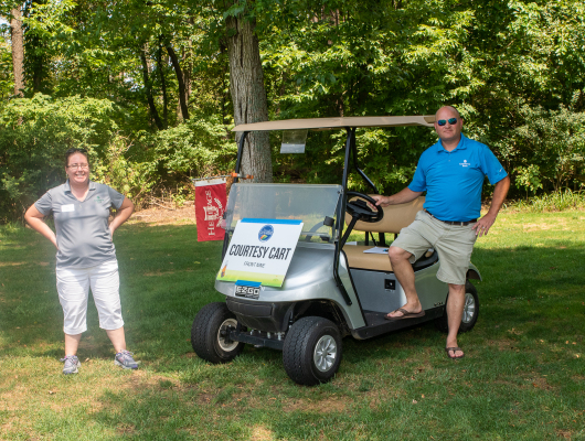 man and woman standing around golf cart